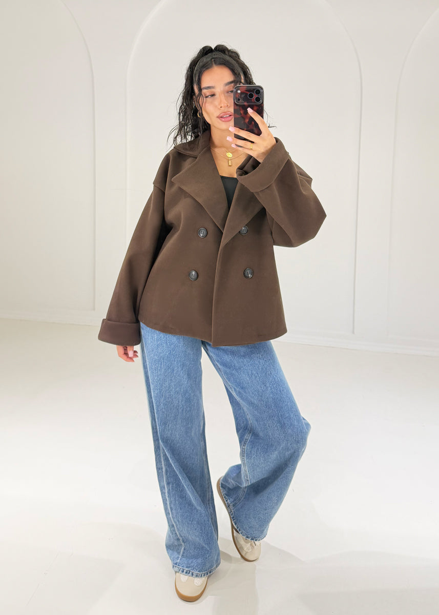 Frau in kurzer schokobrauner Caban Jacke mit Zweireiher-Knöpfen und großem Revers kombiniert mit Wide Leg Jeans und schwarzem Top