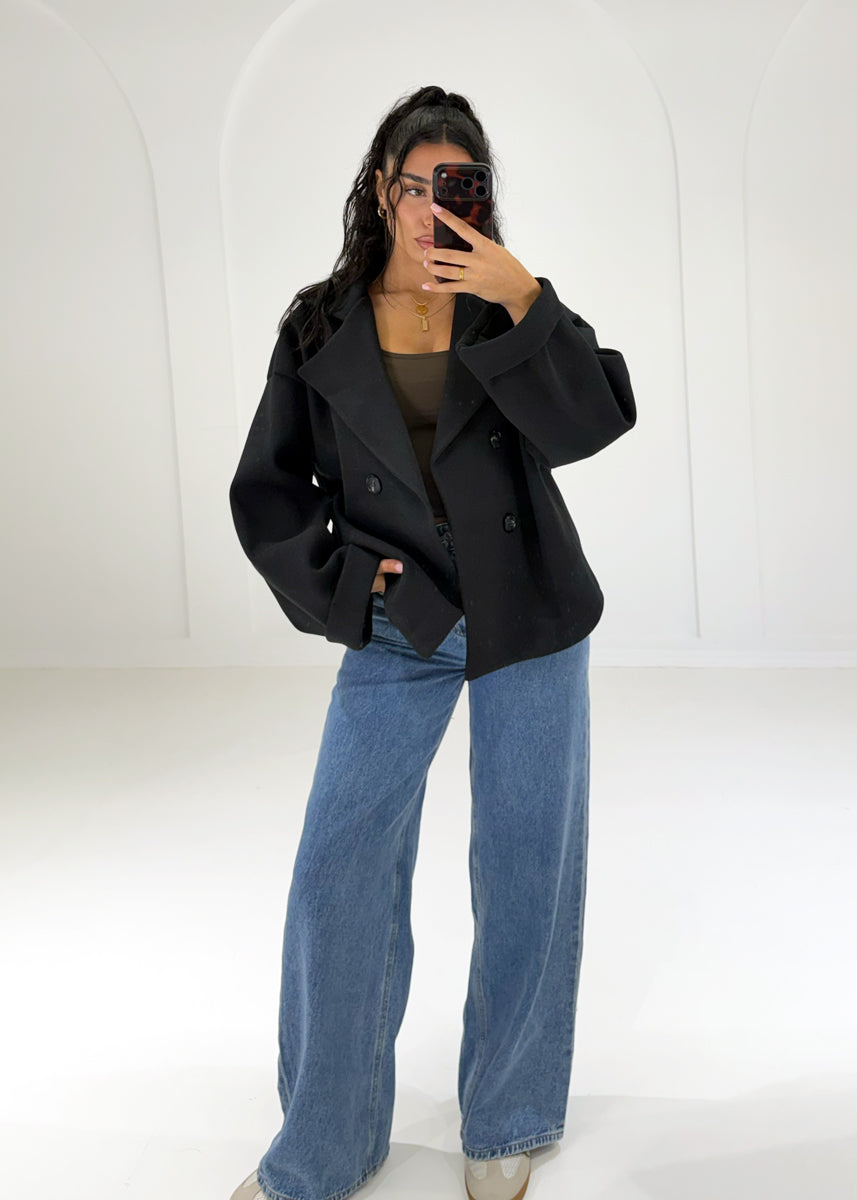 Frau in kurzem schwarzem Zweireiher-Mantel in Woll-Optik zu Wide-Leg-Jeans, Vorderansicht