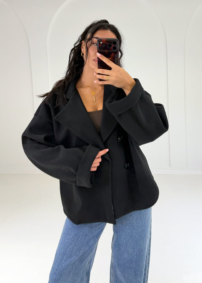 Frau in kurzem schwarzem Zweireiher-Mantel geschlossen zu Wide-Leg-Jeans, Nachaufnahme
