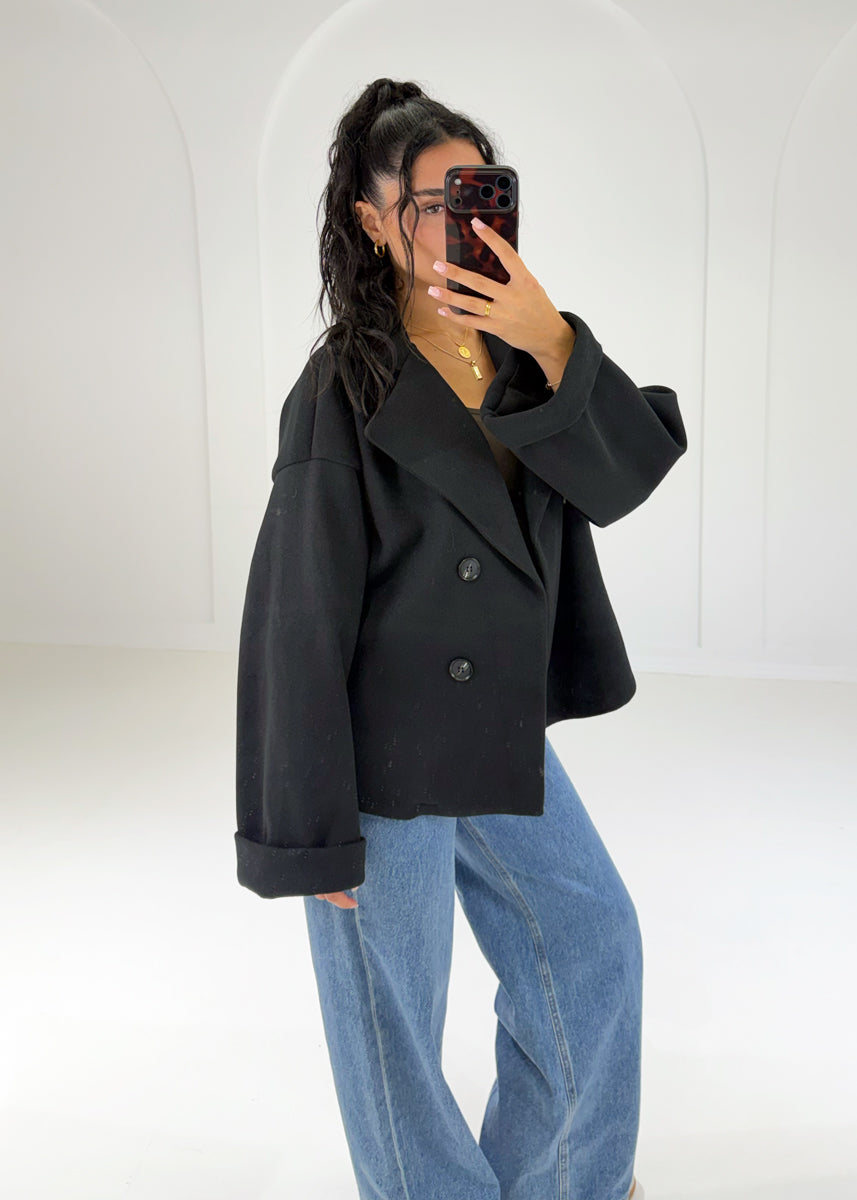 Frau in kurzem schwarzem Zweireiher-Mantel in Woll-Optik zu Wide-Leg-Jeans, Seitenansicht