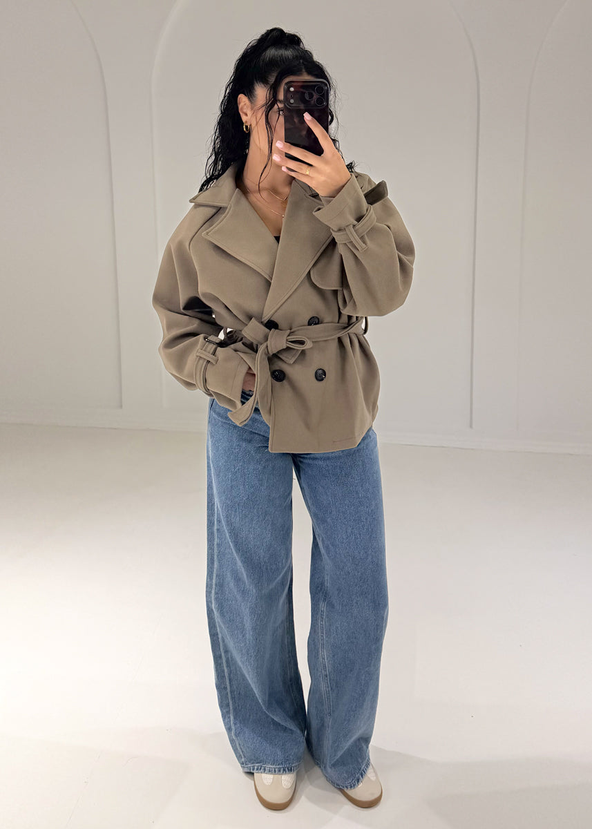 Frau in kurzem Trenchcoat in Taupe mit Bindegürtel zu Wide-Leg-Jeans, Vorderansicht