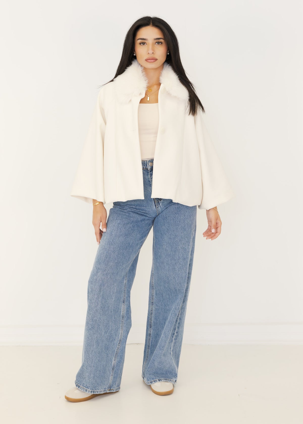 Cremefarbener Kurzmantel mit Kunstfellkragen offen getragen über beigem Top und Jeans
