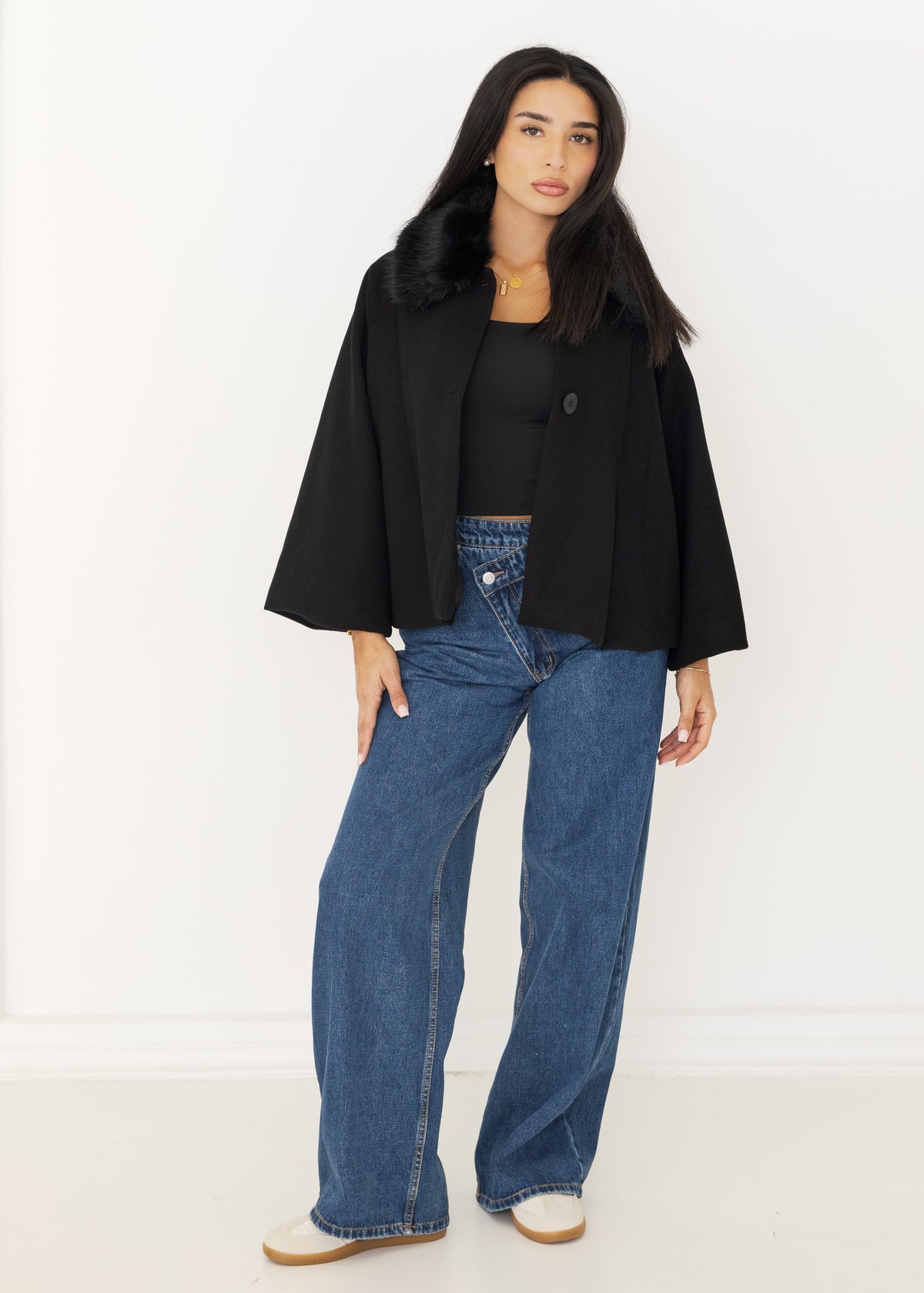 Schwarzer Kurzmantel mit Kunstfellkragen offen getragen über schwarzem Top und Jeans