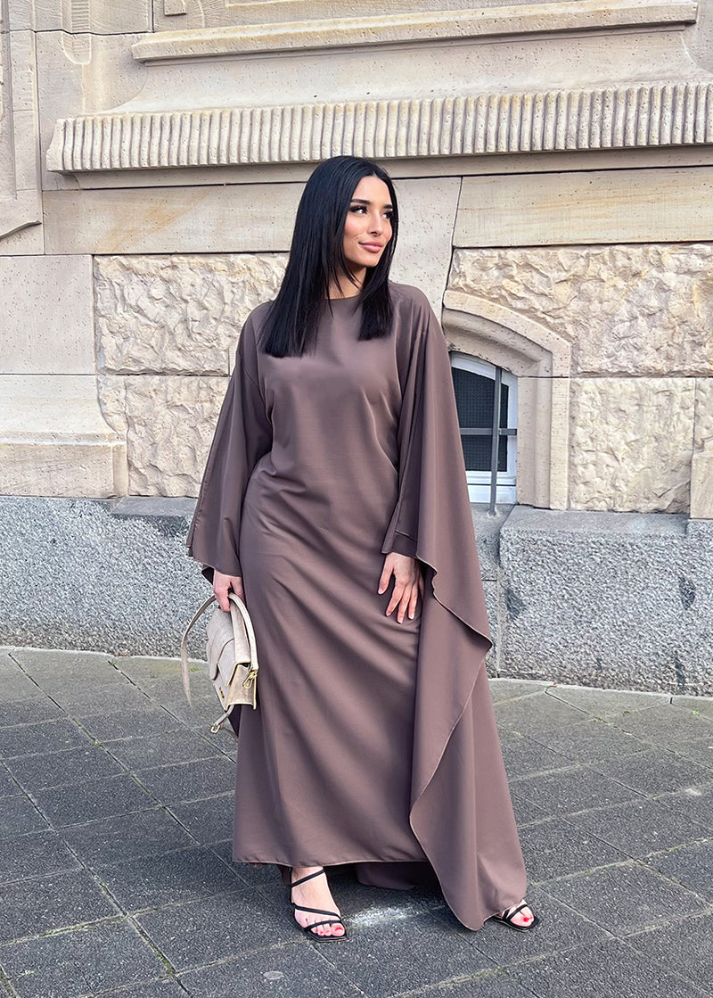 Modell trägt ein tailliertes Maxikleid in Taupe mit fließendem Schnitt und weitem Rock