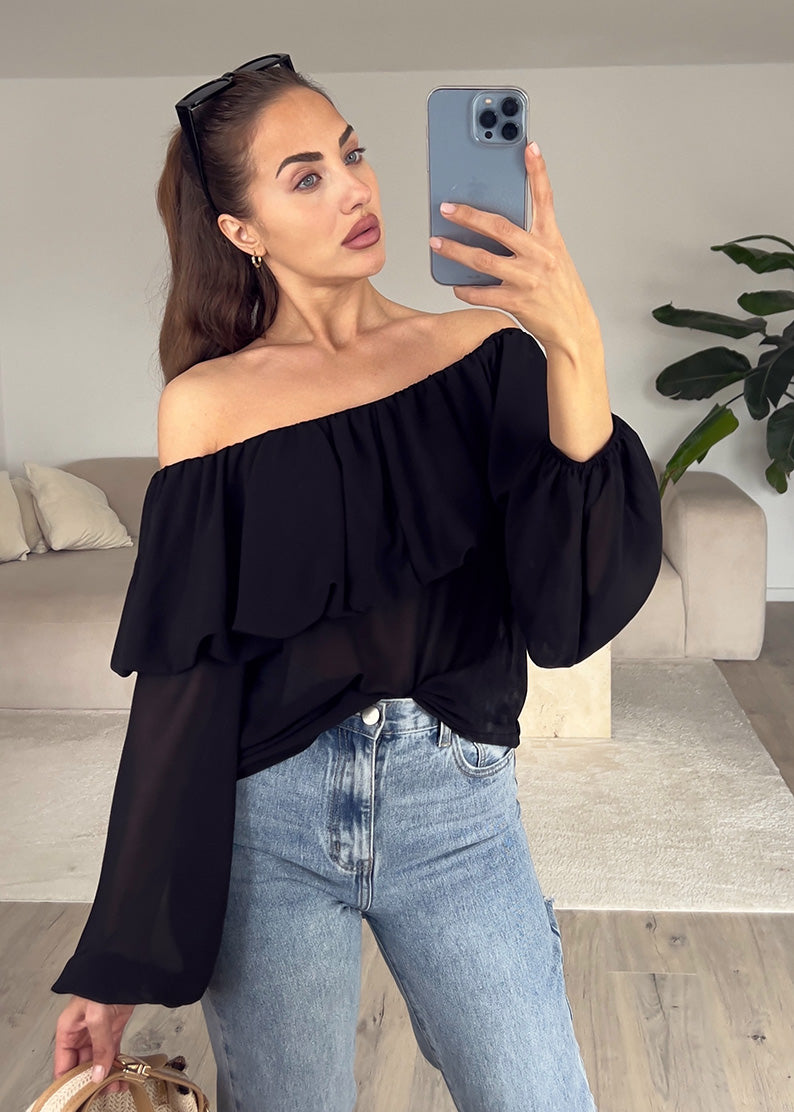 Modell trägt ein schulterfreies Oberteil in Schwarz mit breitem Ausschnitt und figurbetontem Schnitt