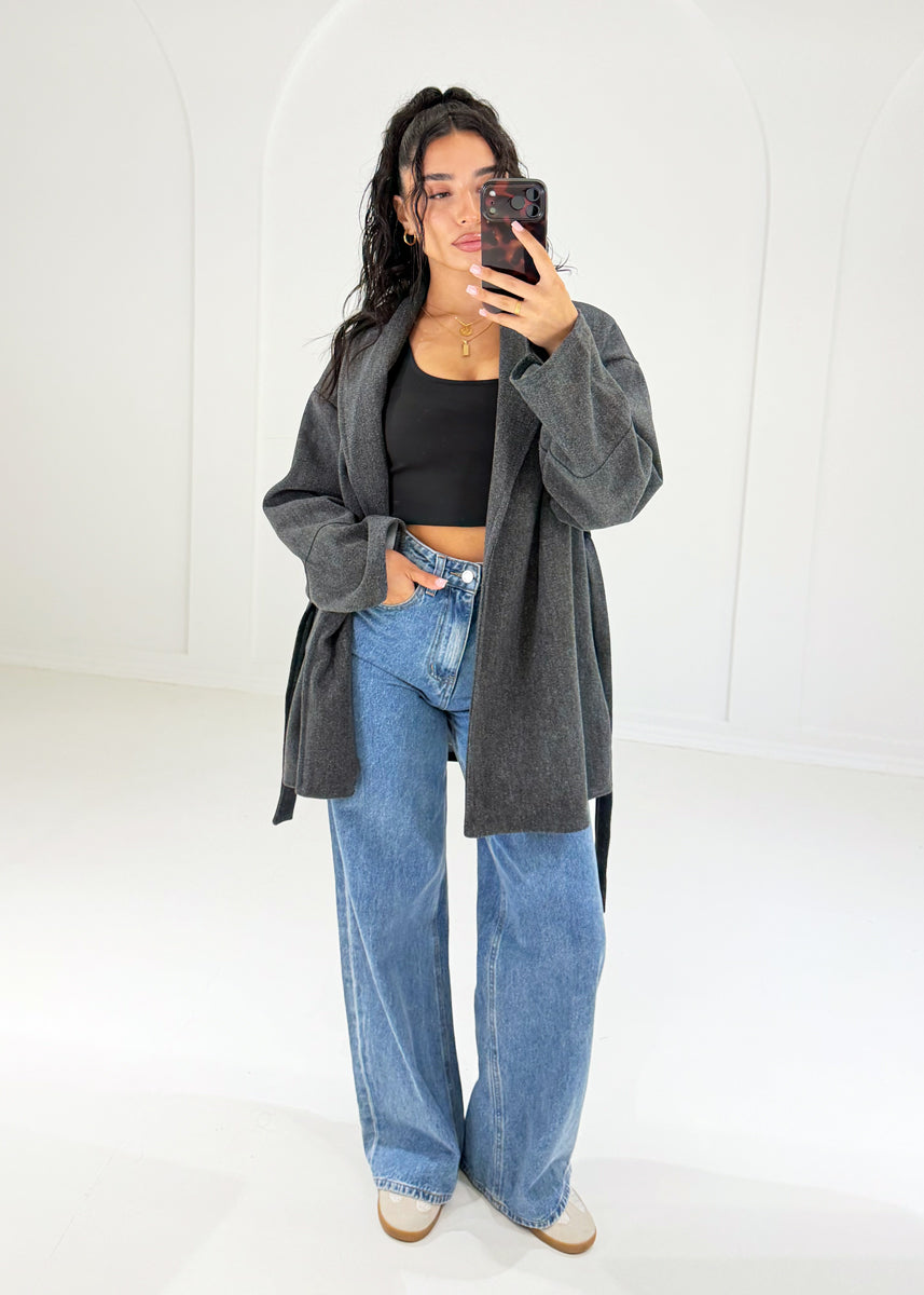 Frau in anthrazitfarbener Wickeljacke mit Bindegürtel zu Wide-Leg-Jeans, Vorderansicht