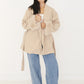 Model hält den Schalkragen der beigen Oversize-Wickeljacke mit flauschigen Fell-Manschetten