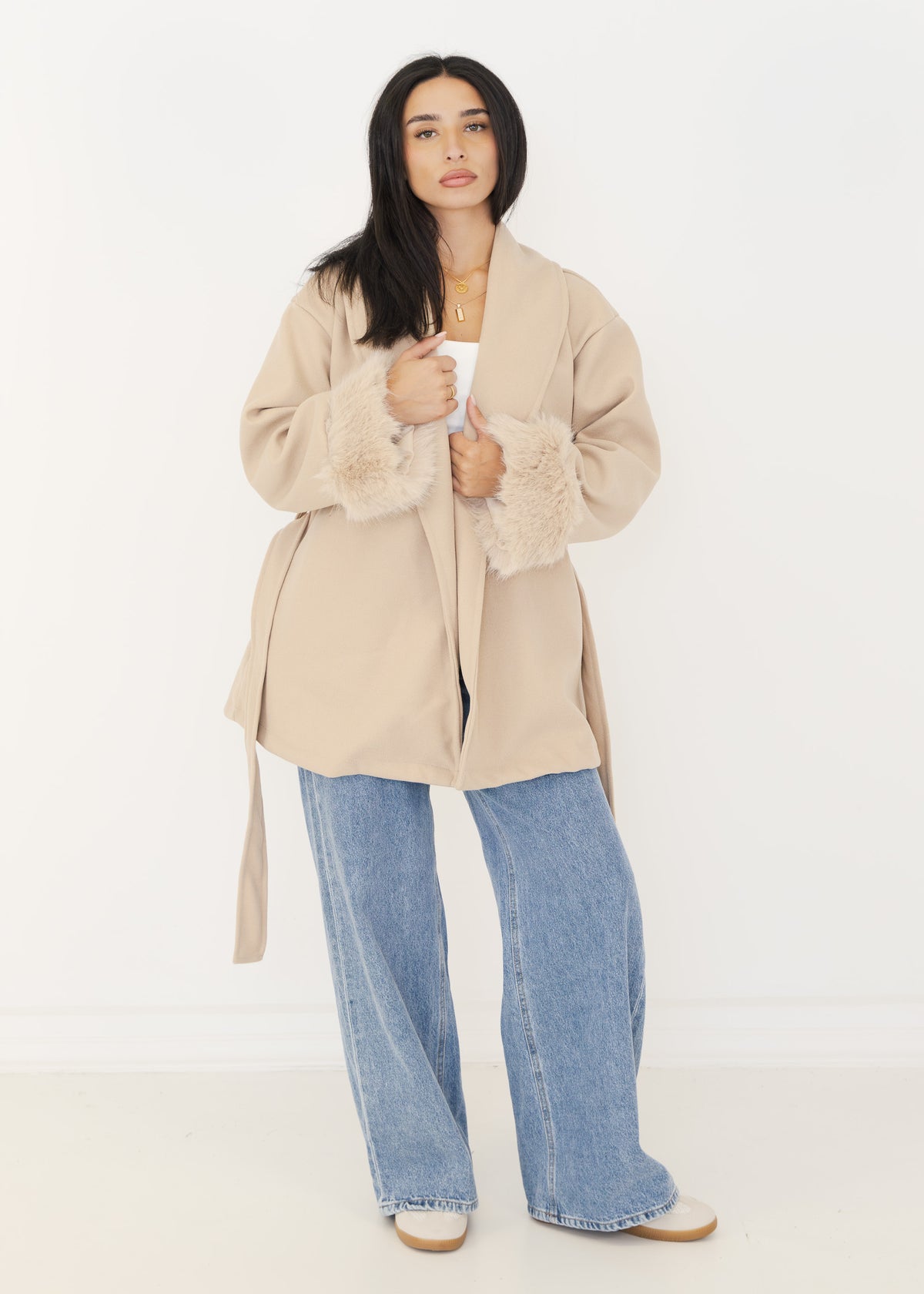 Model hält den Schalkragen der beigen Oversize-Wickeljacke mit flauschigen Fell-Manschetten