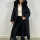 Modell trägt einen langen Damen Steppmantel mit Kapuze und Taillengürtel – NAHA Wintermode
