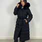 Modell trägt einen langen Damen Steppmantel mit Kapuze und Taillengürtel – NAHA Wintermode