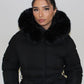 Modell trägt einen langen Damen Steppmantel mit Kapuze und Taillengürtel – NAHA Wintermode