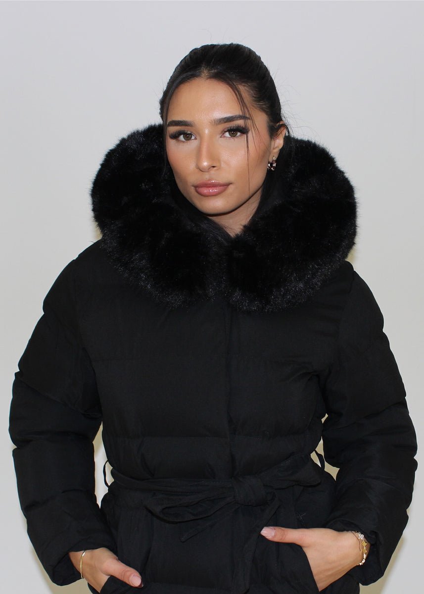 Modell trägt einen langen Damen Steppmantel mit Kapuze und Taillengürtel – NAHA Wintermode
