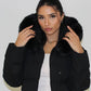 Modell trägt einen langen Damen Steppmantel mit Kapuze und Taillengürtel – NAHA Wintermode