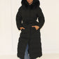 Modell trägt einen langen Damen Steppmantel mit Kapuze und Taillengürtel – NAHA Wintermode