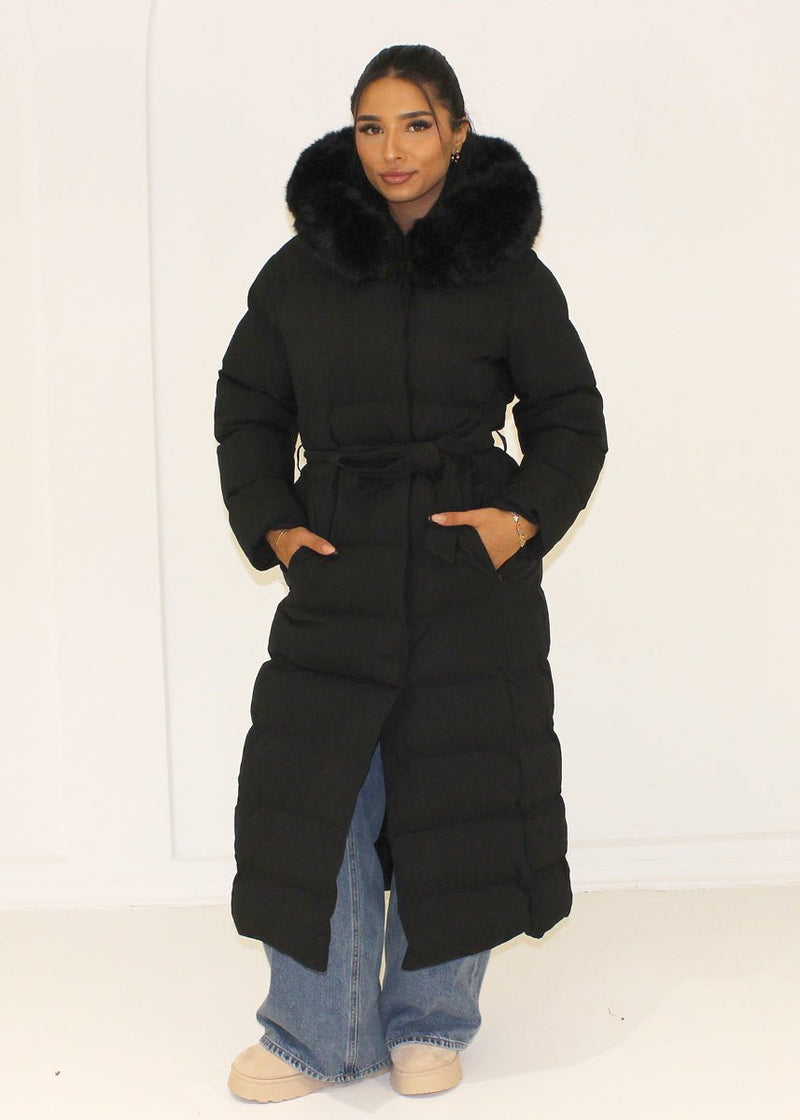 Modell trägt einen langen Damen Steppmantel mit Kapuze und Taillengürtel – NAHA Wintermode