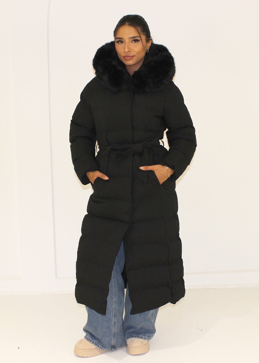 Modell trägt einen langen Damen Steppmantel mit Kapuze und Taillengürtel – NAHA Wintermode