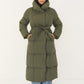 Frau in langem khakifarbenem Puffer Mantel mit Gürtel, Hände in den Taschen