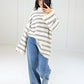 Frau in cremefarbenem Oversize-Ringelpullover mit schwarzen Streifen zu Wide-Leg-Jeans, ganze Figur