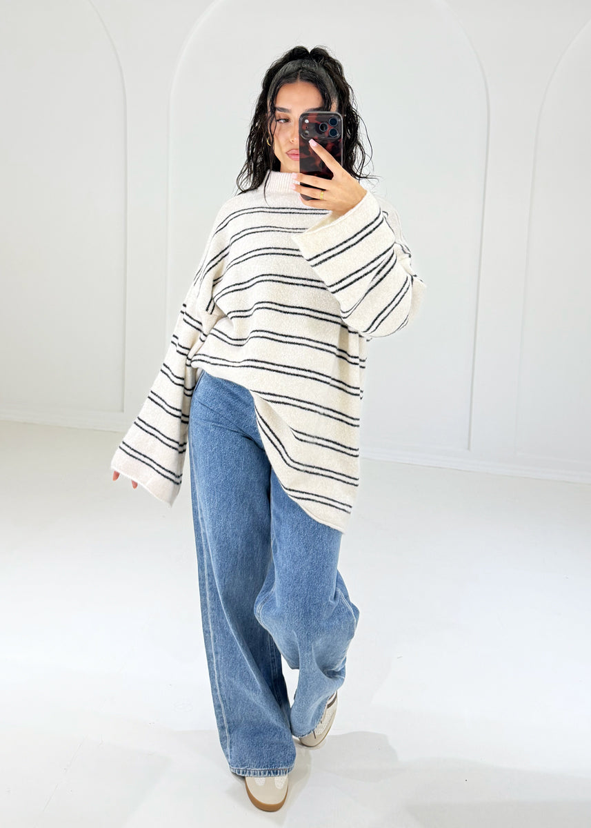 Frau in cremefarbenem Oversize-Ringelpullover mit schwarzen Streifen zu Wide-Leg-Jeans, ganze Figur