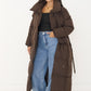 Langer brauner Puffer Coat offen getragen zu schwarzem Top und Jeans