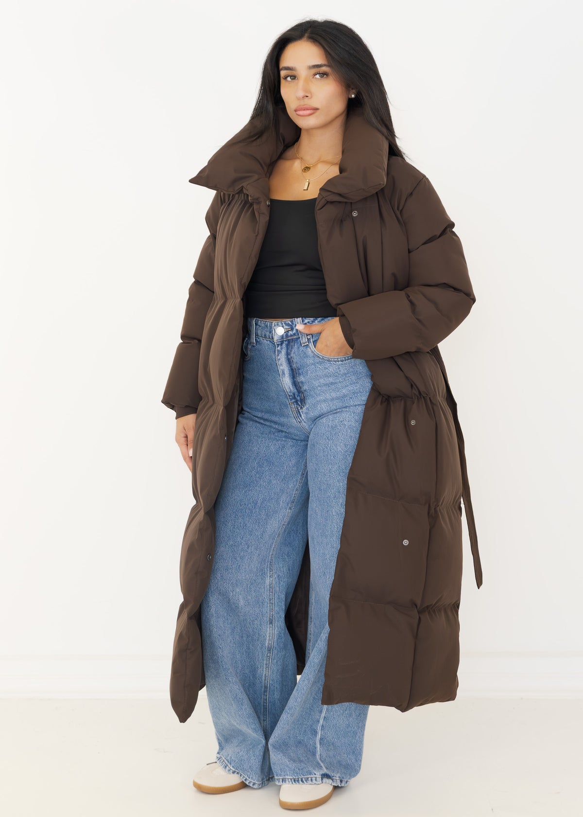 Langer brauner Puffer Coat offen getragen zu schwarzem Top und Jeans