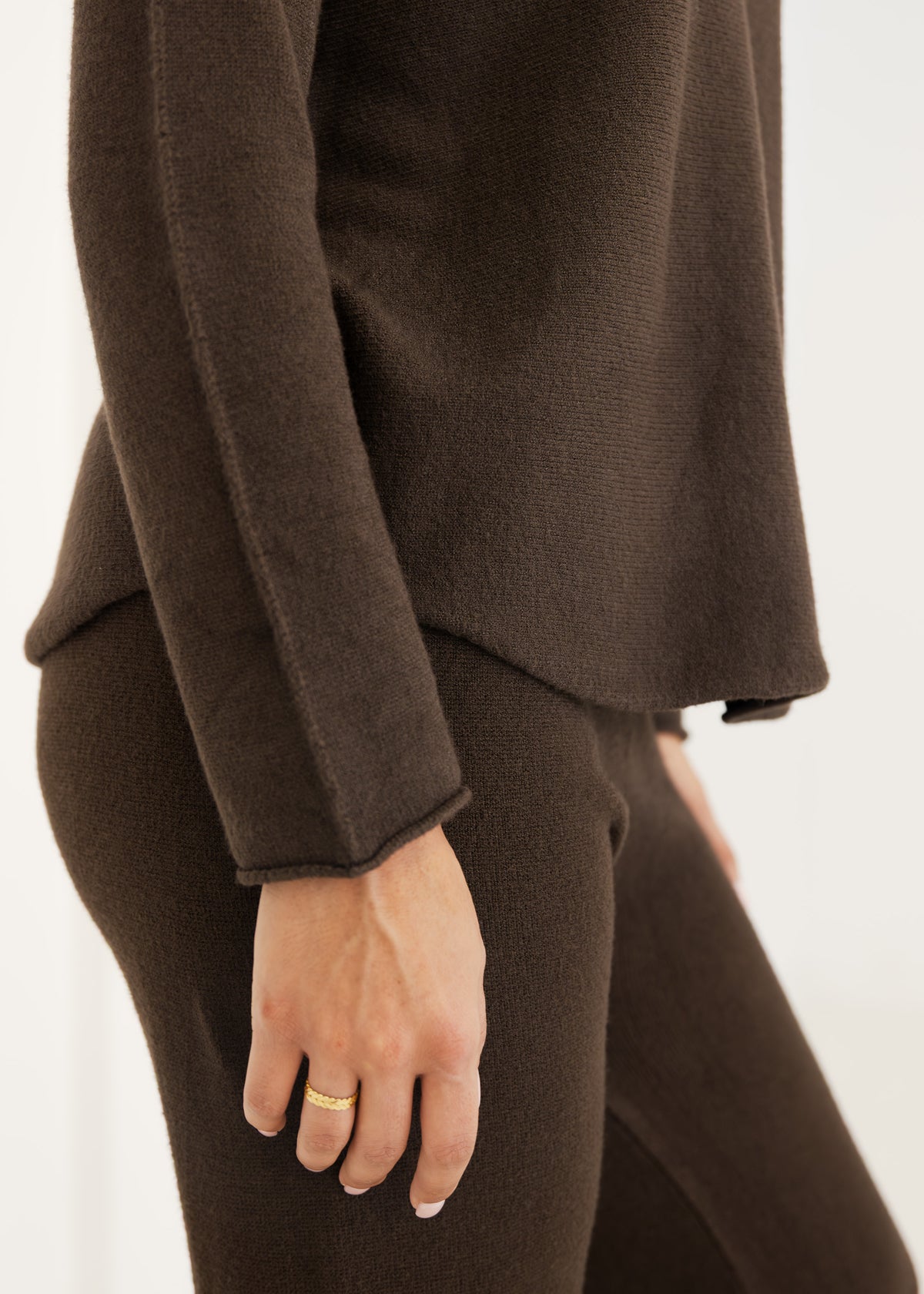 Detailansicht der offenen Rollkante und Ziernaht am Ärmel des dunkelbraunen Strickpullovers