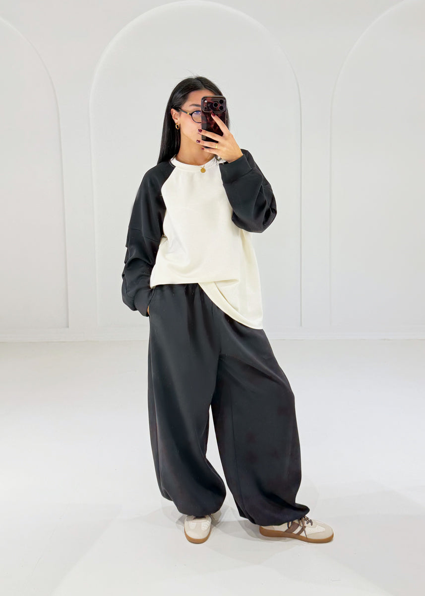 Frau in Oversize-Sweat-Set mit Raglan-Sweatshirt in Creme-Schwarz und weiter schwarzer Ballonhose, ganze Figur