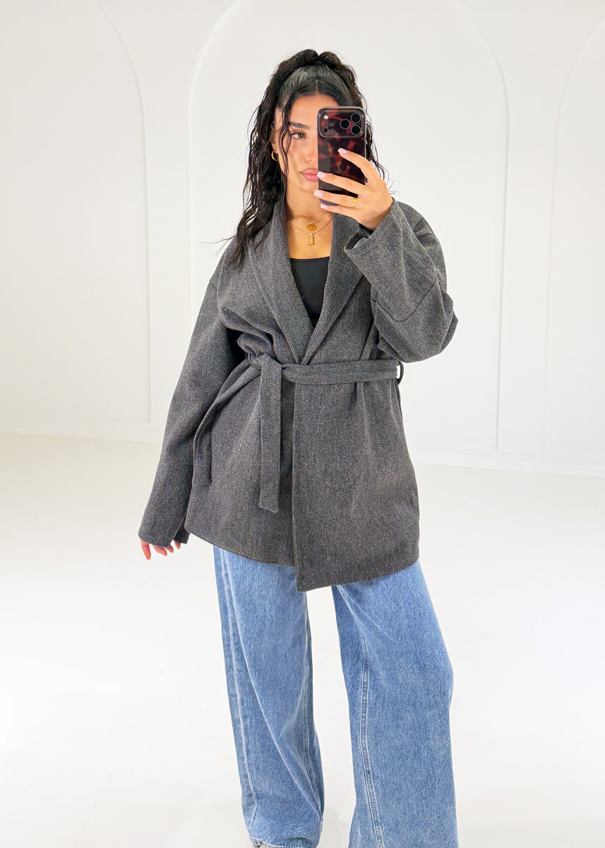 Frau in anthrazitfarbener Wickeljacke mit Bindegürtel zu Wide-Leg-Jeans, Vorderansicht